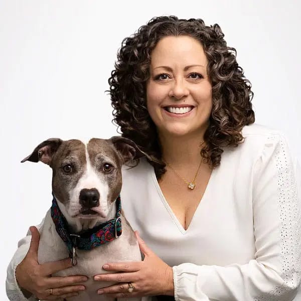 Smiling woman with curly dark hair holding a grey and white dog on a white background