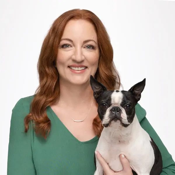 Smiling red-haired woman in a green top holding a black and white dog