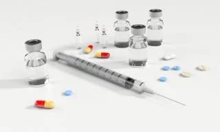 Syringe, small glass vials and loose pills and capsules on a white surface