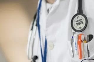 Close-up of a white coat with a stethoscope and pens in the breast pocket