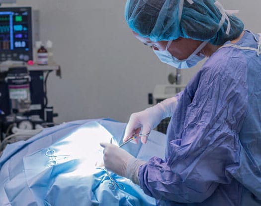 Person in surgical cap, mask and gown working over a blue drape under bright light