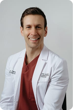 Smiling man with short brown hair in a white coat over maroon scrubs