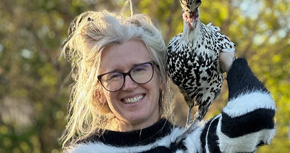 Smiling woman with grey hair and glasses holding a black and white speckled chicken