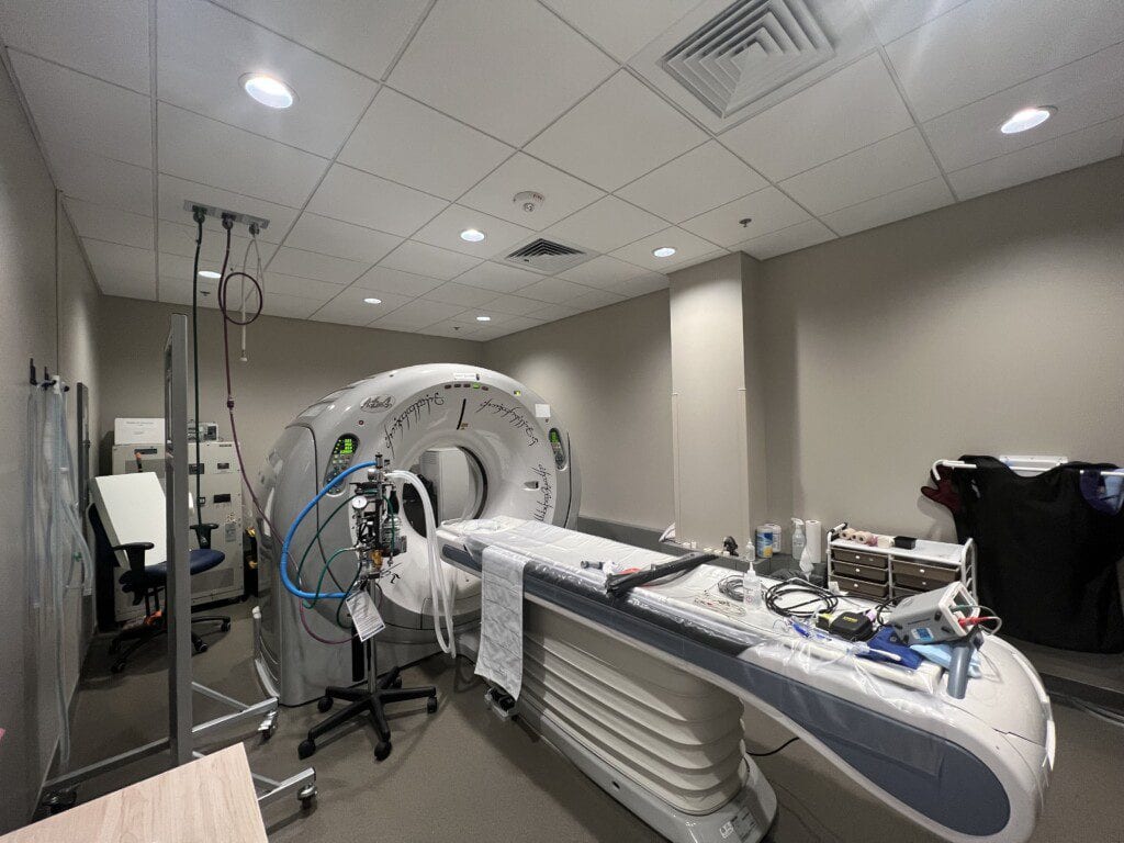 Imaging scanner with a long padded table in a room with ceiling lights and equipment
