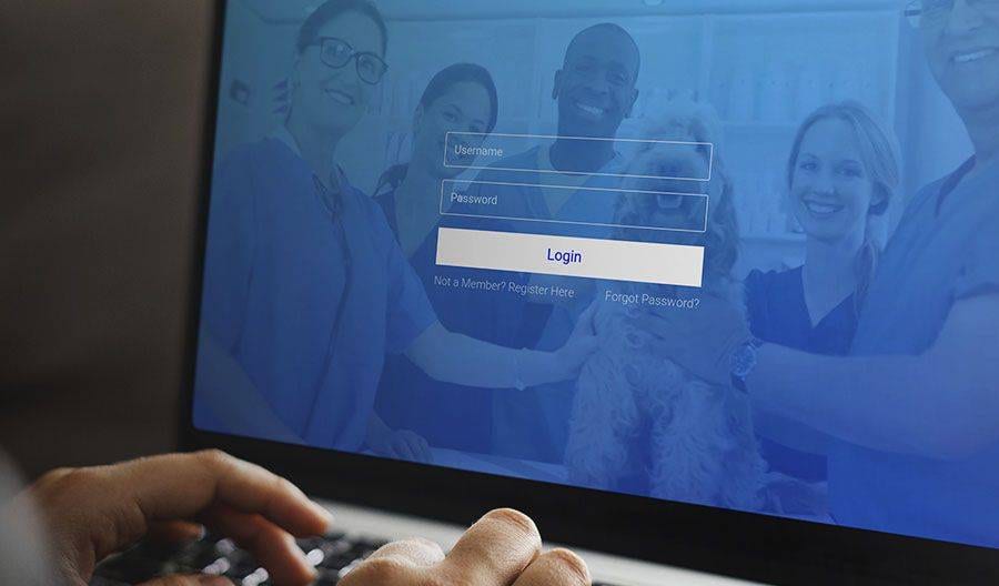 Laptop screen showing a login form over a blue-tinted photo of smiling people in scrubs with a dog