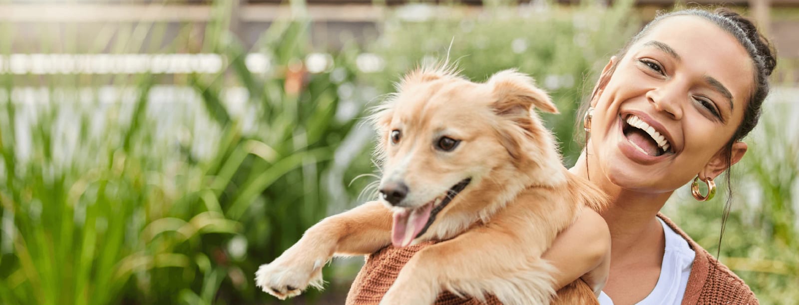 Laughing woman holding a golden-tan dog with its tongue out in a garden