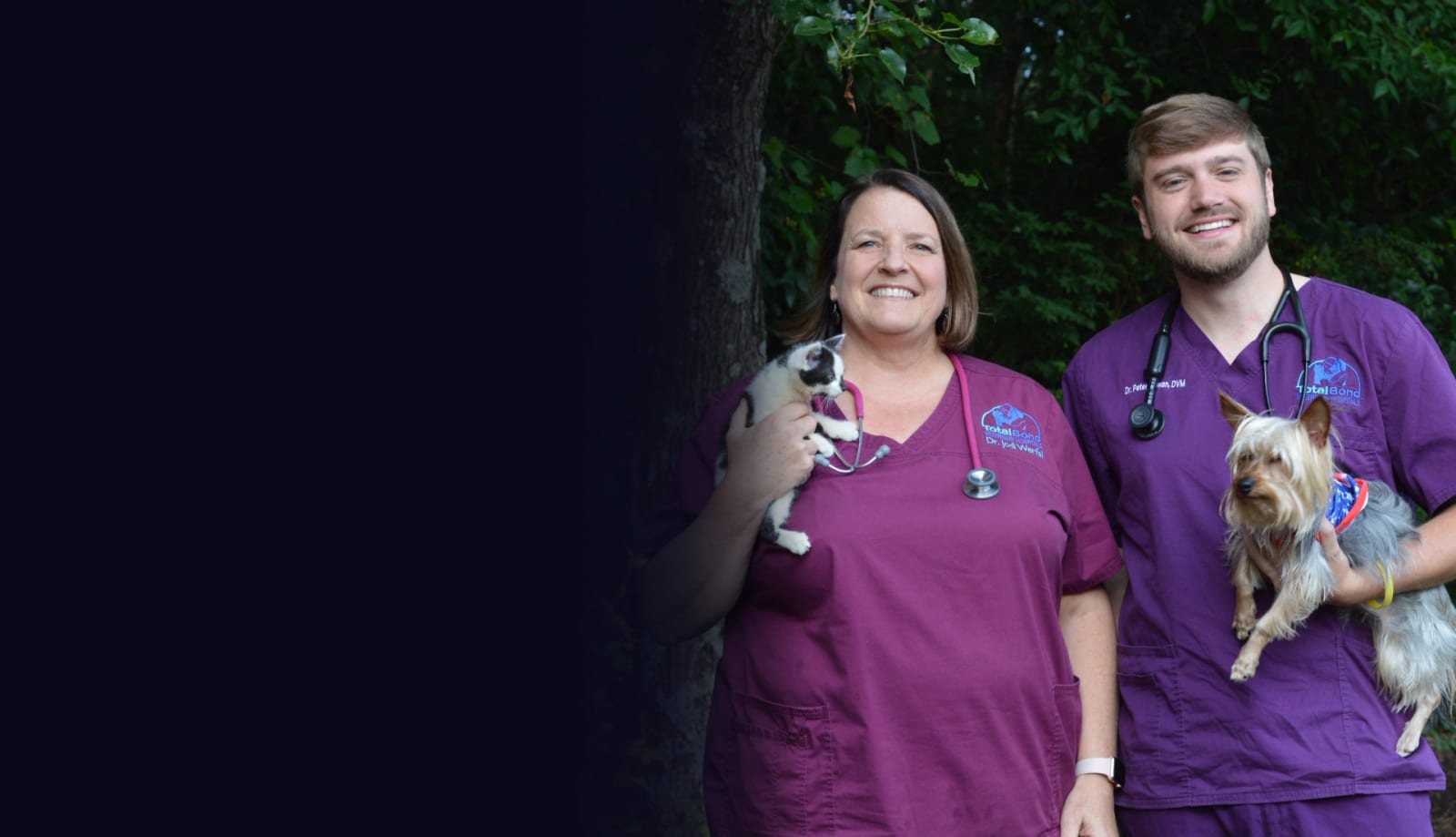 Two people in purple scrubs holding a small black and white dog and a small tan dog outdoors