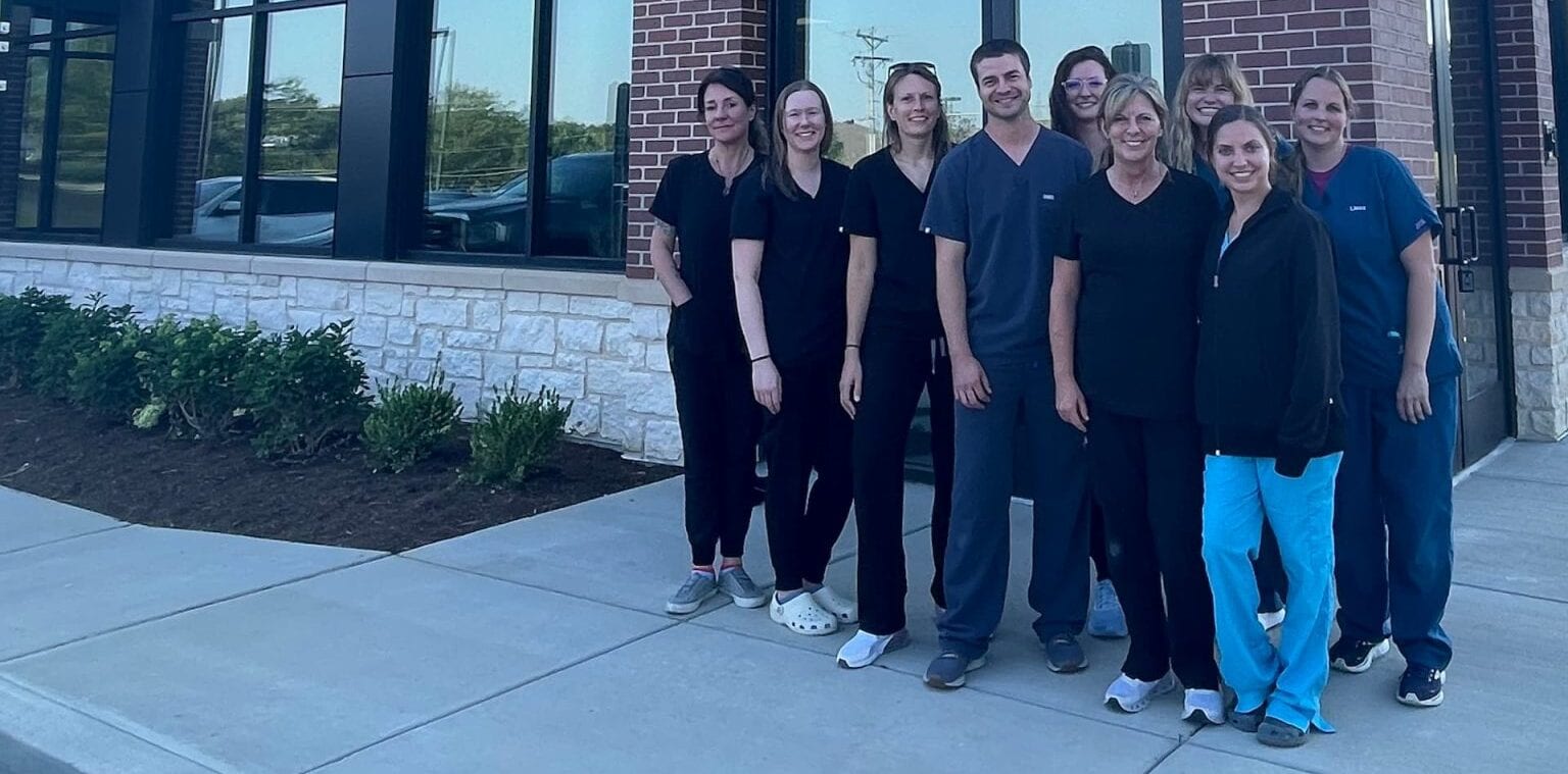 Group of people in scrubs standing together on a sidewalk outside a brick building