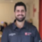 Very small blurry image of a smiling man with a dark beard in a dark polo shirt