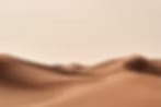 Very small blurry image of sand dunes under a pale beige sky