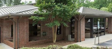 Red brick building with metal roofs, a courtyard tree and glass doors beside a parking area