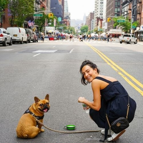 Smiling woman crouching on a city street beside a tan dog on a leash