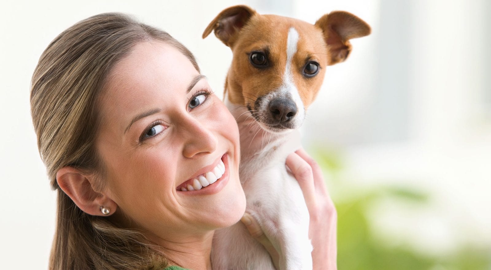 Smiling woman holding a small brown and white dog up beside her face