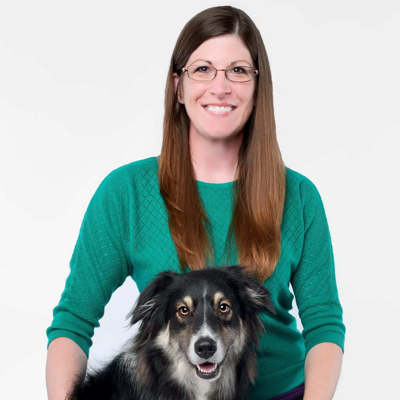 Smiling woman with long hair and glasses in a green sweater with a black and tan dog in front