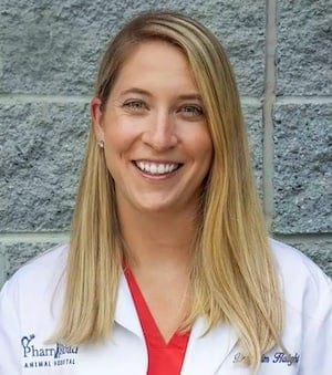 Smiling woman with long blonde hair in a white coat over a red top in front of a stone wall