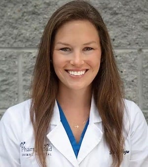Smiling woman with long brown hair in a white coat with a Pharr Road Animal Hospital logo