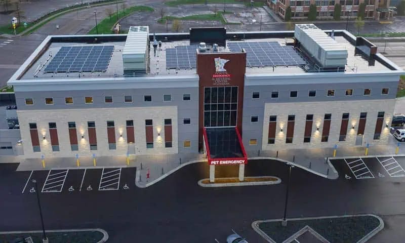 Large grey multi-storey building with rooftop solar panels and a red pet emergency entrance at dusk