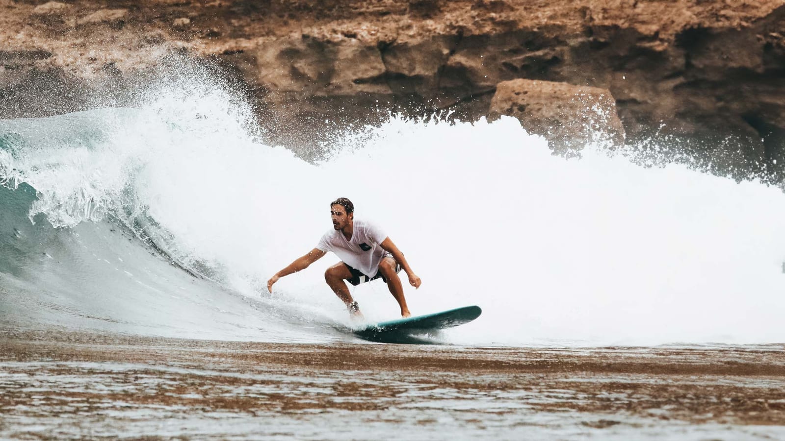 Surfer in a white shirt riding a large breaking wave on a dark green board