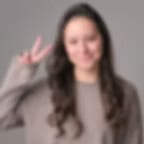 Heavily blurred portrait of a person with long dark hair raising two fingers on a grey background