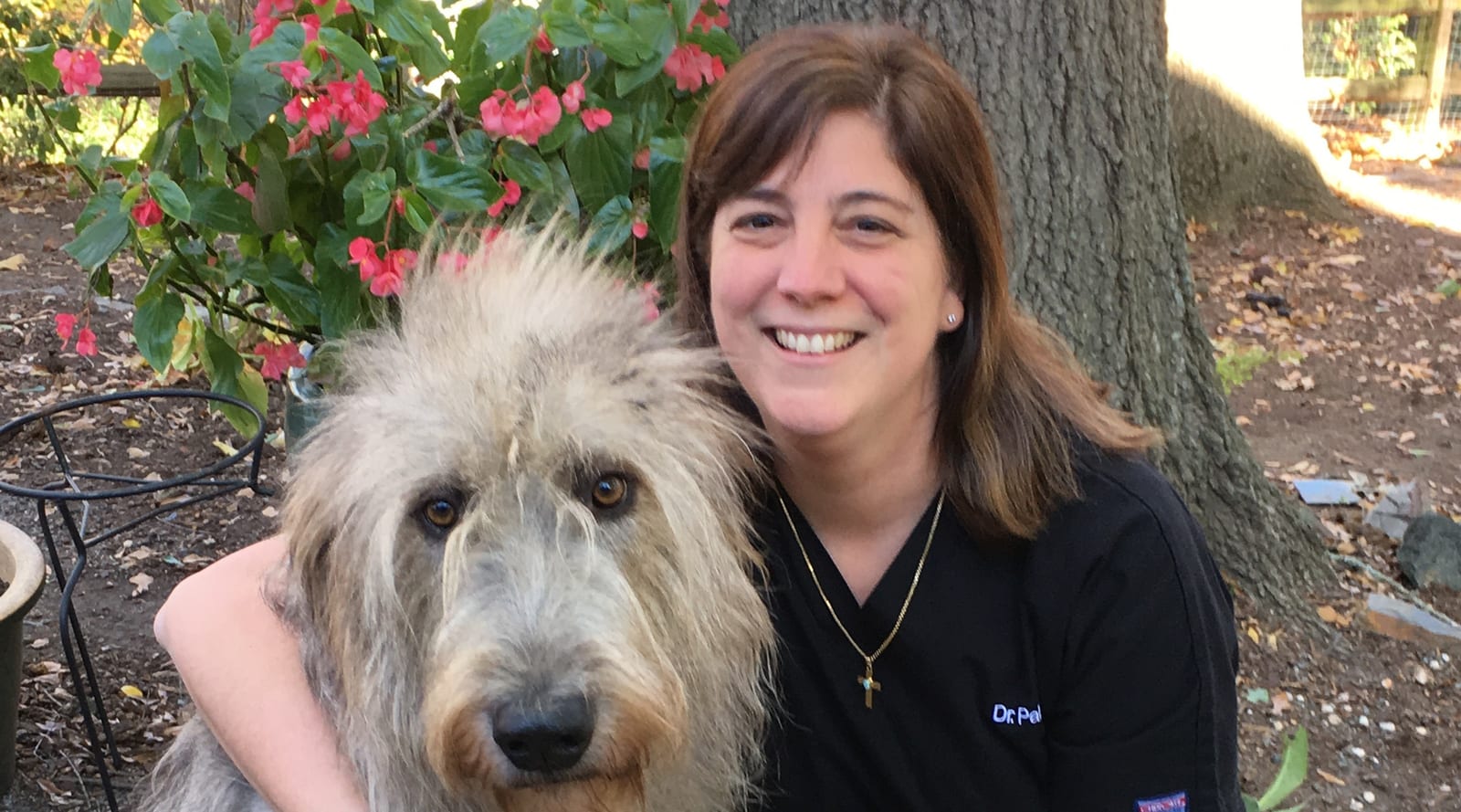 Smiling person in black scrubs hugging a large shaggy grey dog outdoors