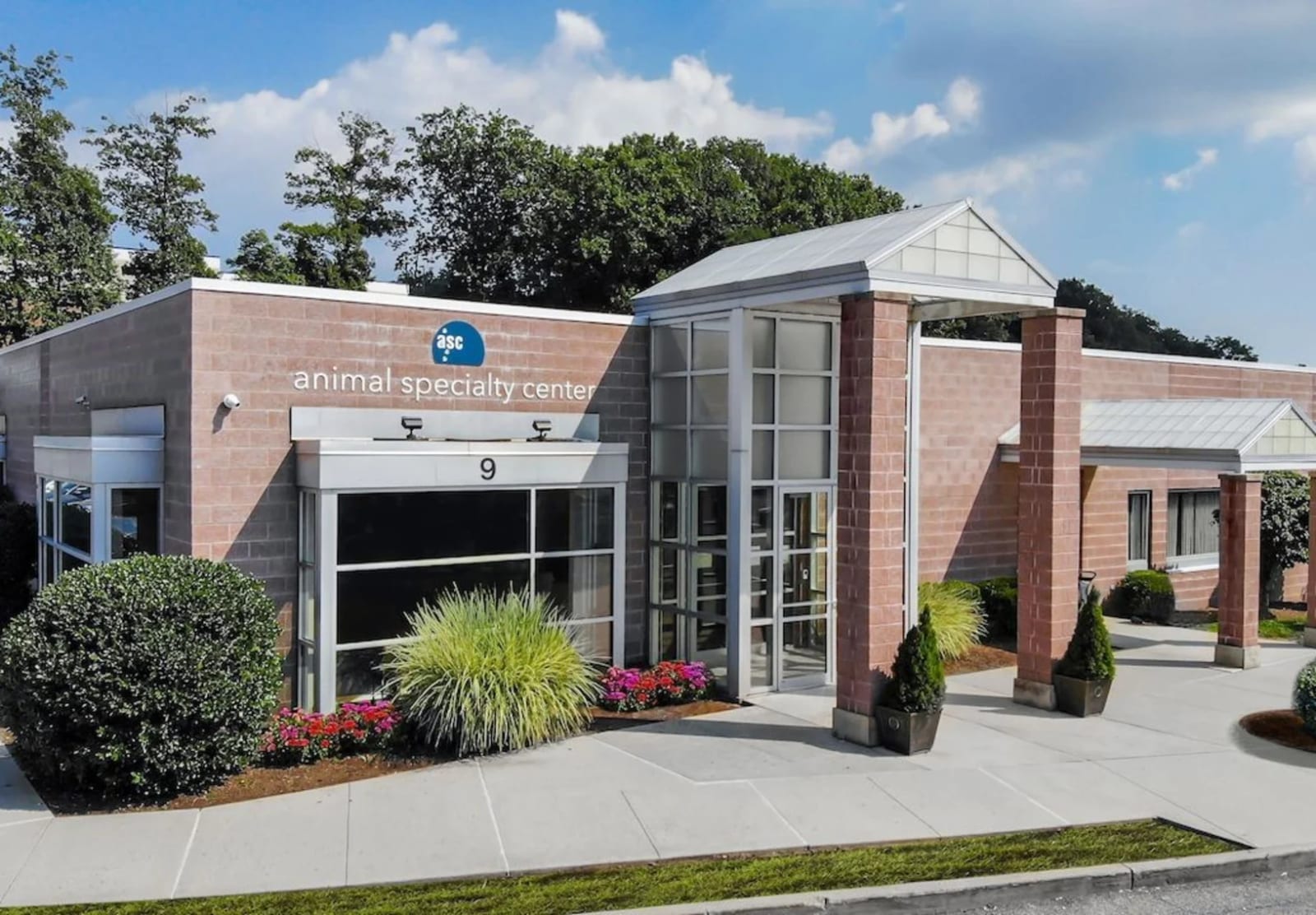 Animal Specialty Center brick building with a glass entrance, a round logo sign and landscaped shrubs