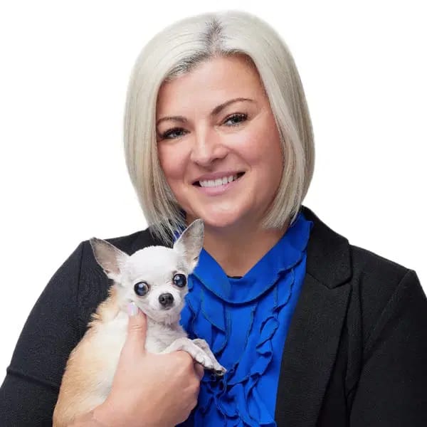 Smiling woman with short silver-blonde hair holding a small white and tan dog
