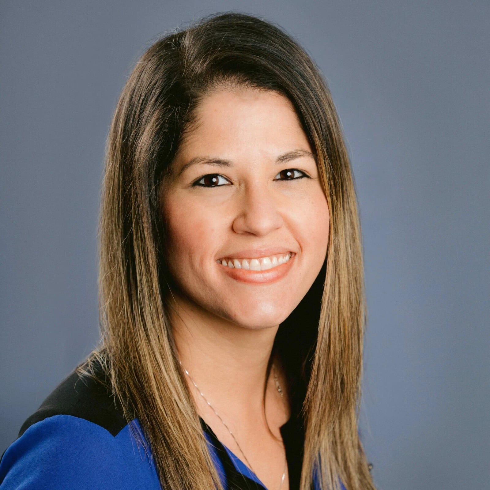 Smiling woman with long brown hair in a blue top against a grey background