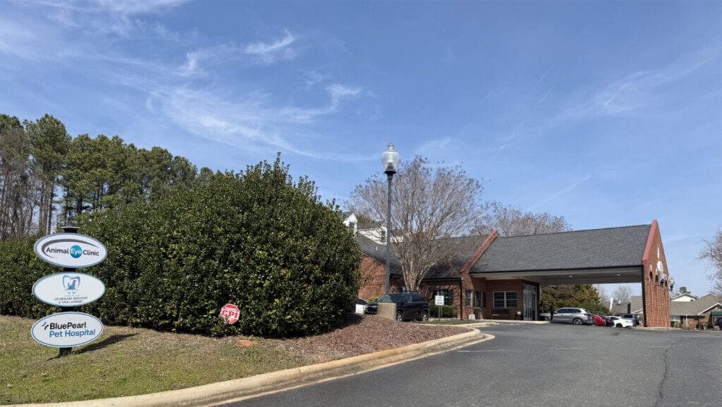 Driveway leading to a brick building with a covered entrance and round signs on a post