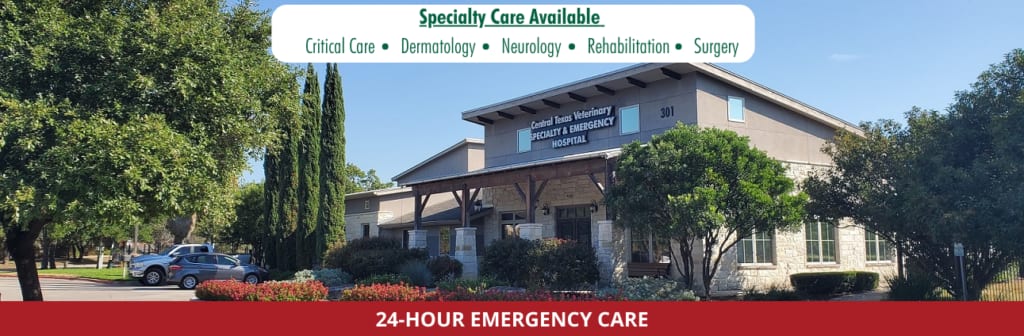 Tan building with a covered entrance under banners reading Specialty Care Available and 24-Hour Emergency Care
