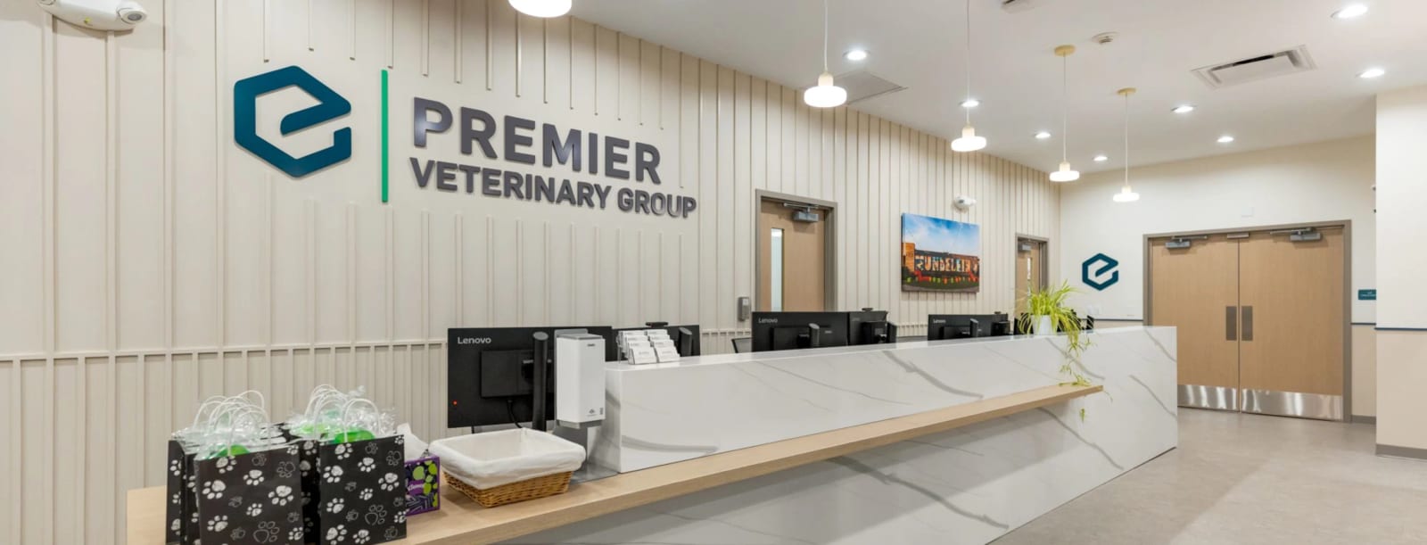 Reception area with a long white counter, computers and a Premier Veterinary Group logo on the wall